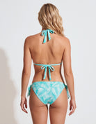 A woman shown from the back wearing a turquoise and white tropical leaf print bikini with tie straps, set against a plain white studio background.