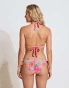 A woman shown from the back wearing a colorful floral bikini with tie straps, photographed against a plain light gray studio background.