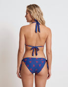 A woman shown from the back wearing a blue string bikini with a red lobster print, set against a plain light gray studio background.