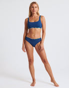A woman modeling a two-piece bikini set in a solid navy blue color, featuring a scoop neck top and matching high-cut bottoms, against a plain white studio background.