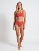 A woman modeling a two-piece coral red bikini set against a plain white studio background.