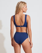 A woman shown from the back wearing a navy blue two-piece swimsuit against a light gray studio background.