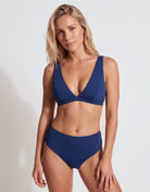 A woman modeling a solid navy blue two-piece bikini set against a clean, light gray studio background.