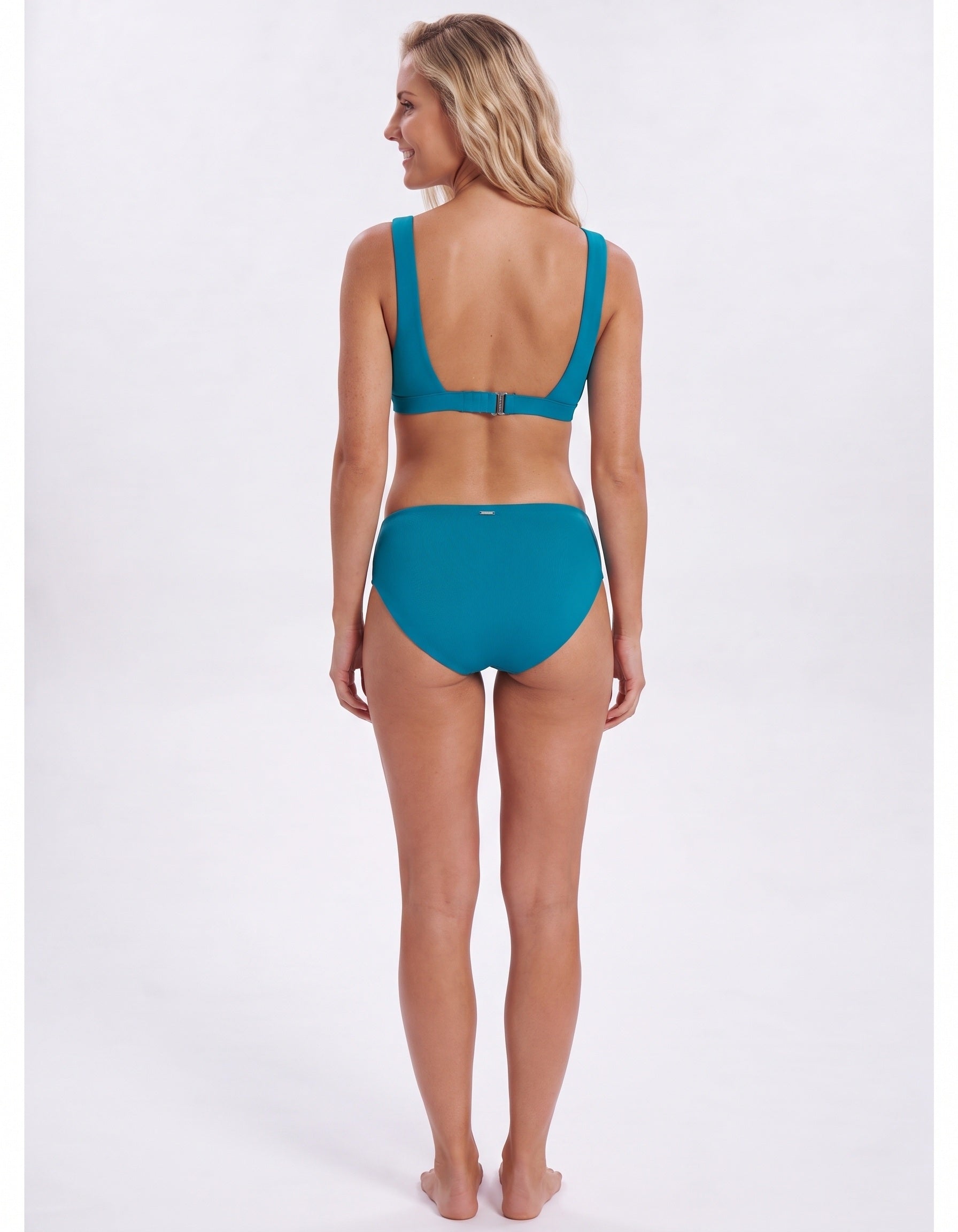 A woman shown from the back wearing a teal two-piece bikini against a plain light gray studio background.