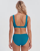 A woman viewed from the back wearing a teal two-piece bikini with a scoop open back and high-waisted bottoms, against a light gray studio background.