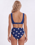 A woman shown from the back wearing a two-piece swimsuit. The top is solid royal blue with a small center buckle, and the high-waisted bottoms are blue with a white sea turtle print.