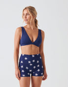 A woman modeling a navy blue two-piece activewear set featuring a crossover sports bra and high-waisted shorts with a white star pattern, set against a plain light gray studio background.