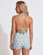 A woman shown from the back wearing a light aqua halter bikini top and matching high-waisted shorts with a pink flamingo print, against a plain white studio background.