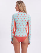 A woman shown from the back wearing a long-sleeve swim top with a pink flamingo print on a light aqua background and solid coral side panels, paired with matching coral bikini bottoms, against a plain white studio background.