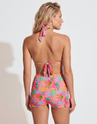 A woman shown from the back wearing a colorful floral halter bikini top and matching high-waisted shorts against a plain light gray studio background.