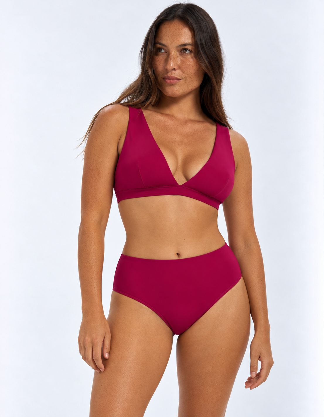 A woman modeling a two-piece bikini set in a plum color, consisting of a scoop-neck triangle top and high-waisted bottoms, against a light gray studio background.