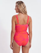 A woman shown from the back wearing a one-piece swimsuit with a bright pink and orange tropical leaf pattern against a plain white studio background.