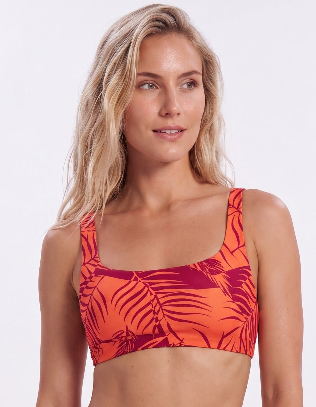 A woman modeling a two-piece bikini swimsuit with a vibrant orange and dark red tropical leaf print against a plain white studio background.